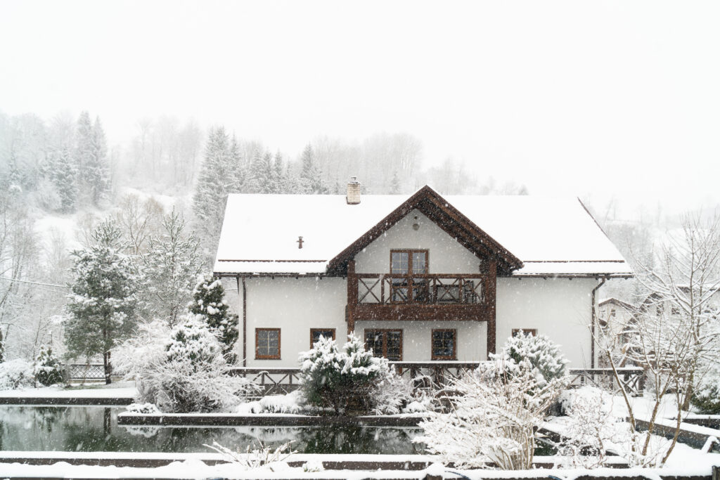 Verschneites Wohnhaus im Winter mit schneebedecktem Dach, Bäumen und Garten.