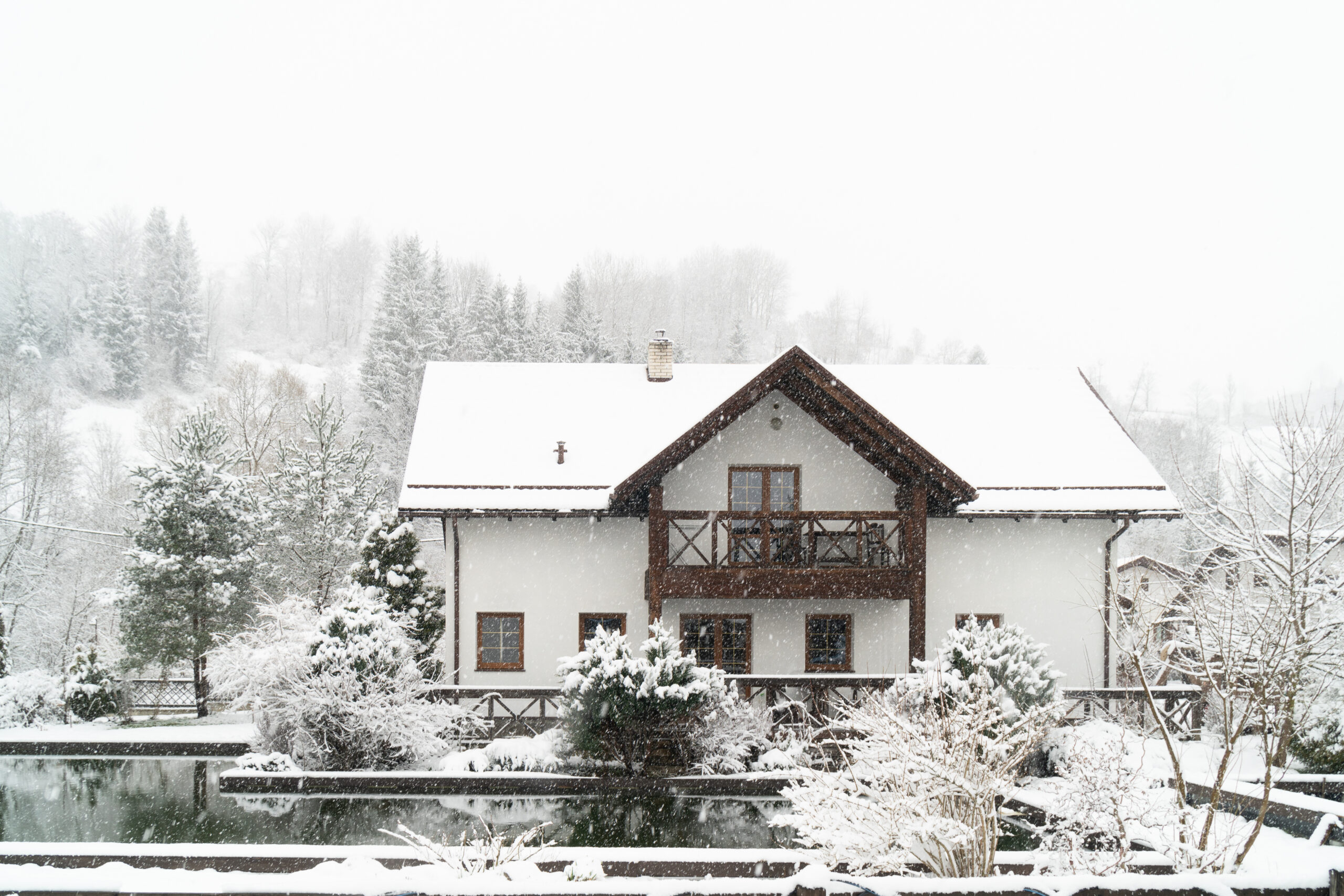 Verschneites Wohnhaus im Winter mit schneebedecktem Dach, Bäumen und Garten.